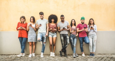 multiracial friends using smartphone against wall at university college backyard young people addicted by mobile smart phone technology concept with always connected millennials filter image