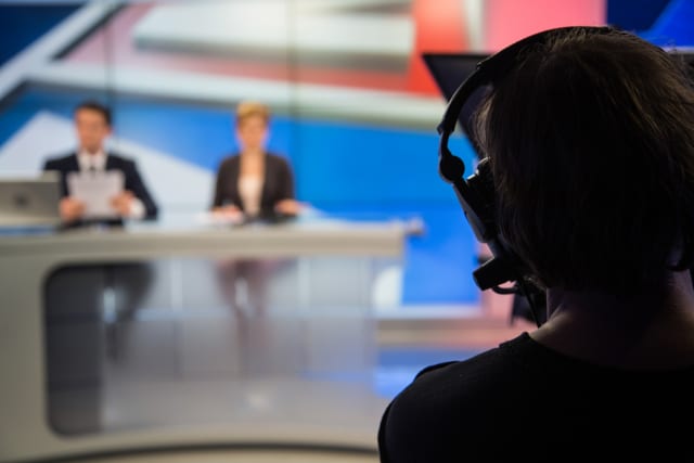 Cameraman filming news presenters in television studio.