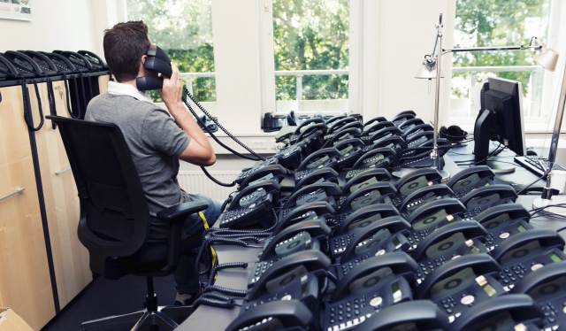 photo of Man busy answering lots of phone calls from a desk with many phones on it
