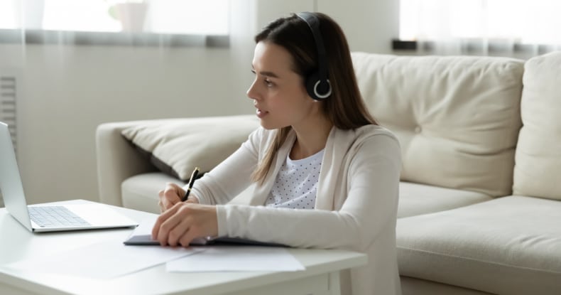 focused woman in headphones watch webinar on laptop writing notes