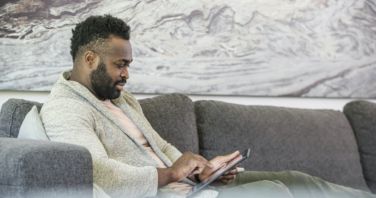man on a grey sofa is interacting with a digital tablet while working from home