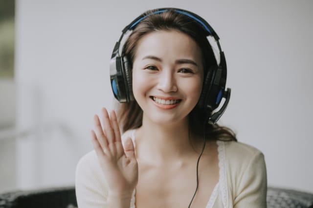 photo of a woman wearing headphones smiling and waving as if on a video conferencing call