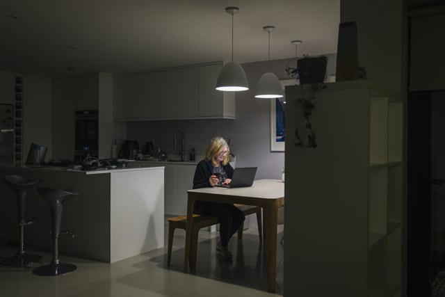 woman working at her kitchen table at night on her laptop