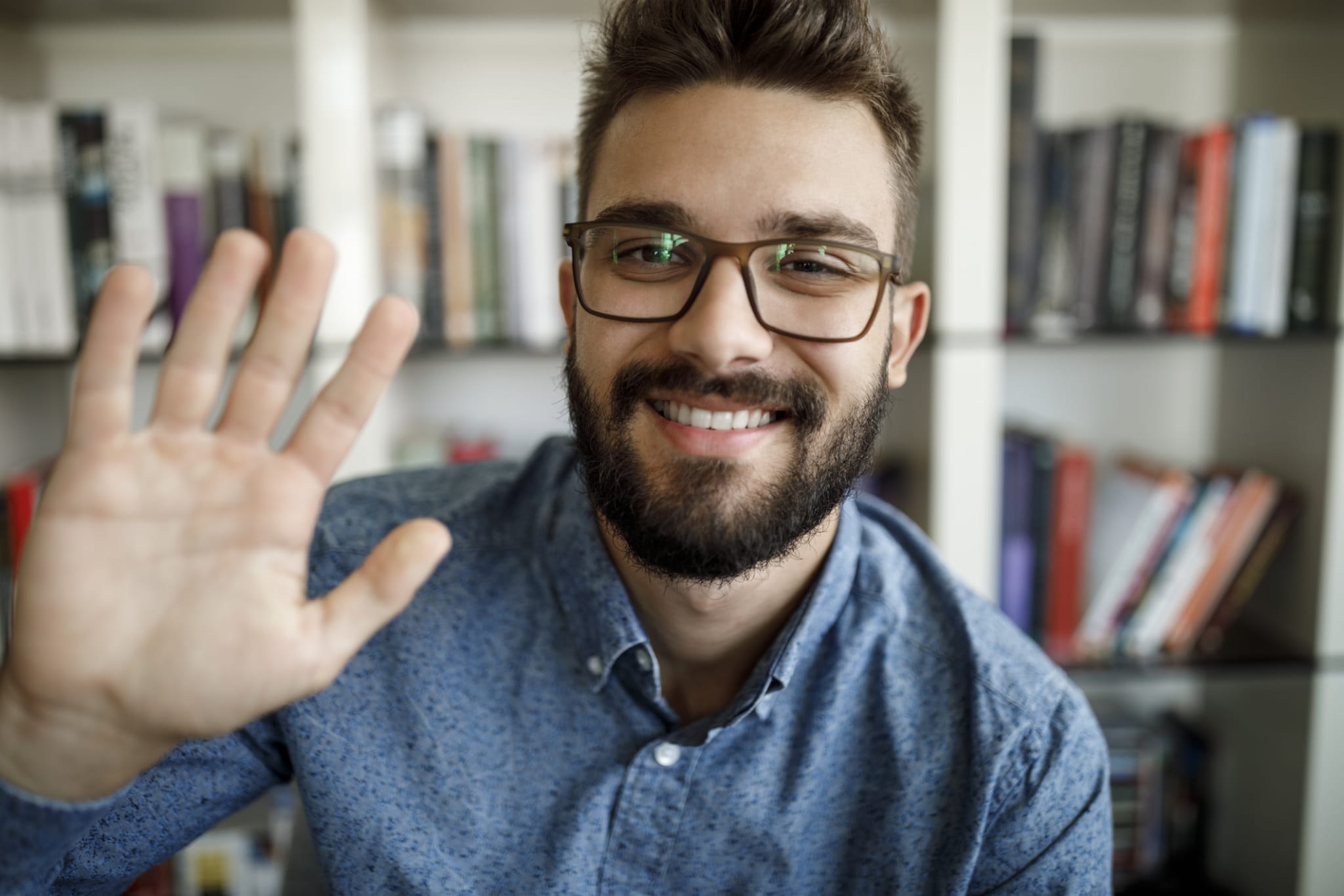 man waving with hand on video call at home office