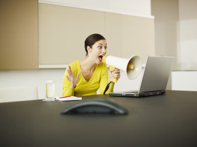 Businesswoman yelling at laptop with bullhorn in conference room